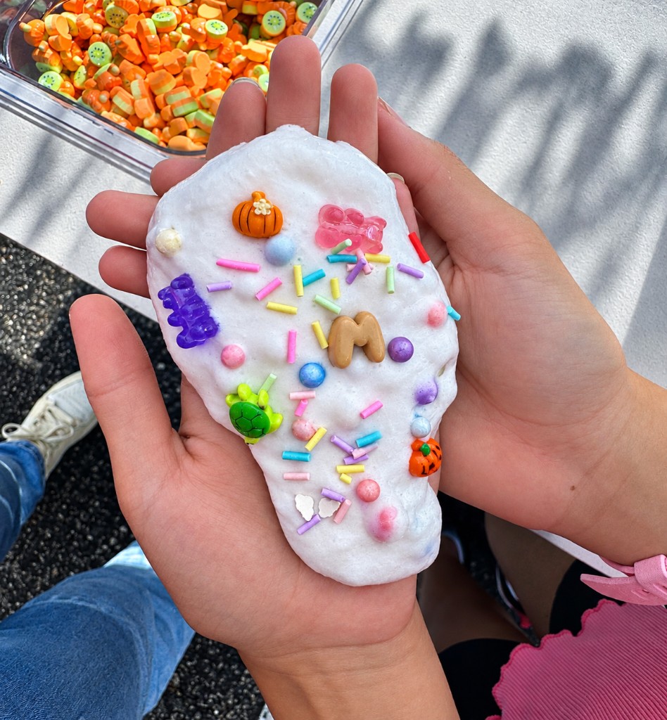 Hands holding white slime topped with sprinkles, gummy candies, and charms
